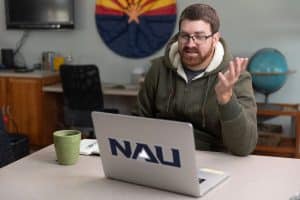 A man sits in front of a laptop taking an online class.