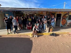 Students pose outside a brightly colored building with a large butterfly painted around the door.